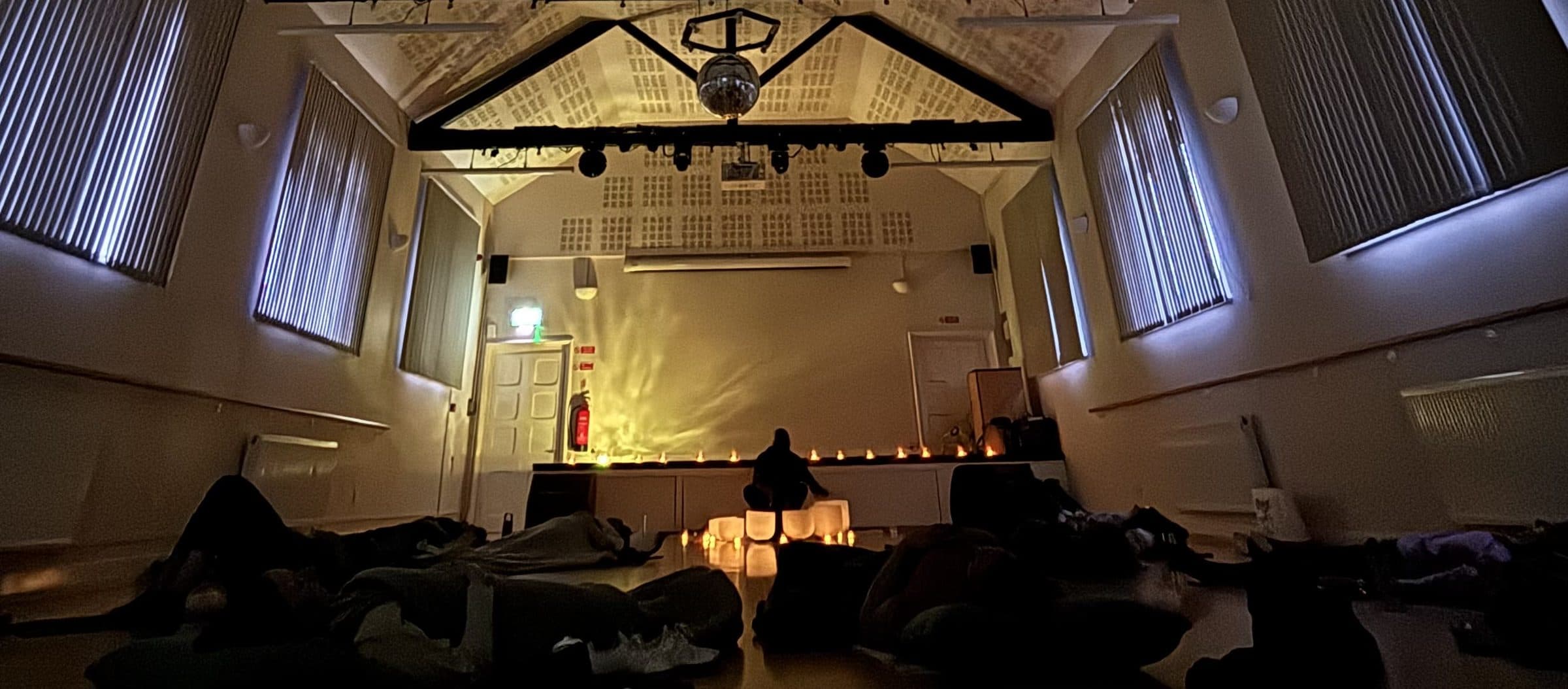 The darkened hall during the sound bath, everyone lying wrapped in blankets facing a line of candles